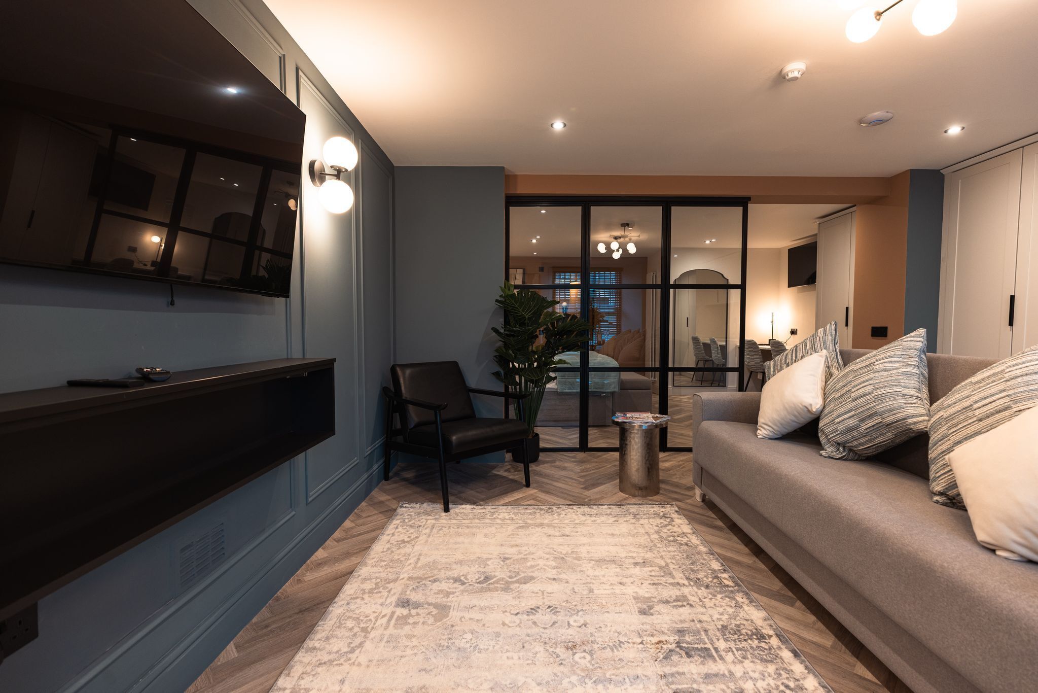Een moderne woonkamer met een bank, fauteuil en een aan de muur bevestigde televisie.