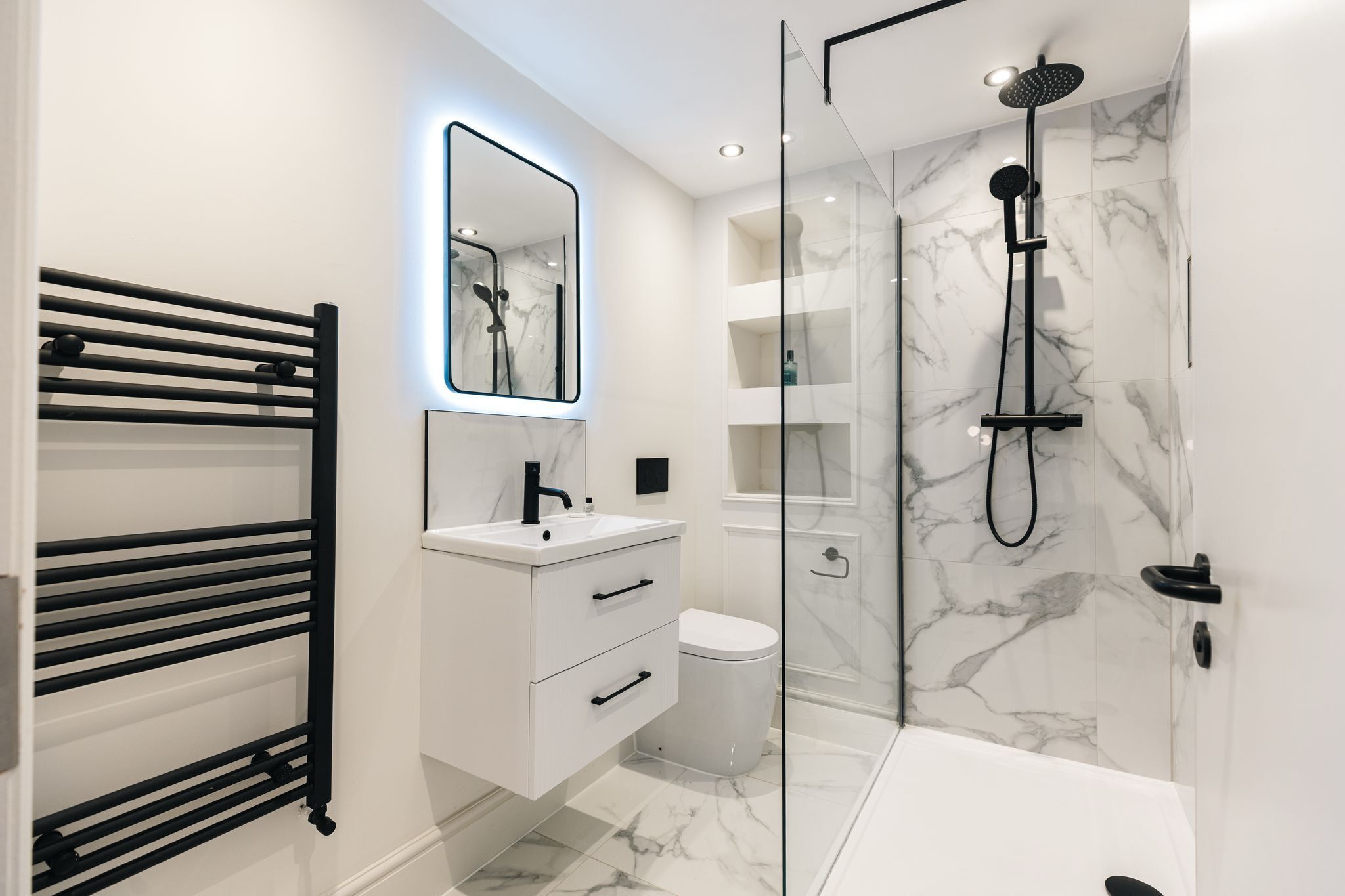 Un baño moderno con ducha envuelta en vidrio, tocador blanco con espejo y toallero negro.
