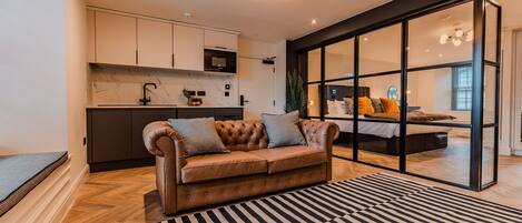 A modern living room with a leather sofa, a black and white striped rug, and a kitchen area with white cabinets and a black countertop.