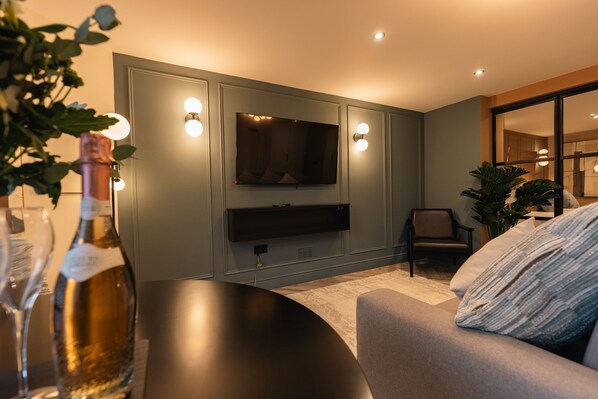 A modern living room with a flat-screen TV mounted on the wall, a dark coffee table, and a comfortable sofa with a textured throw pillow. - Luxury Georgian Aparthotel by Hauss Ayr - 5mins to Beach, Town Centre! (Ayr)