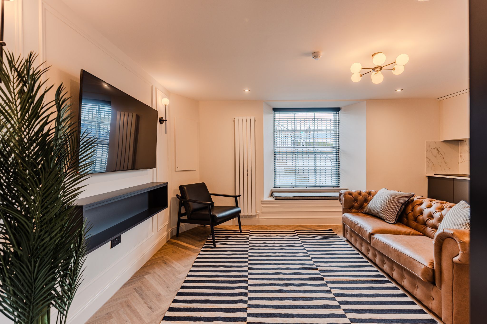 A modern living room with a sofa, a chair, a large mirror, and a patterned rug.