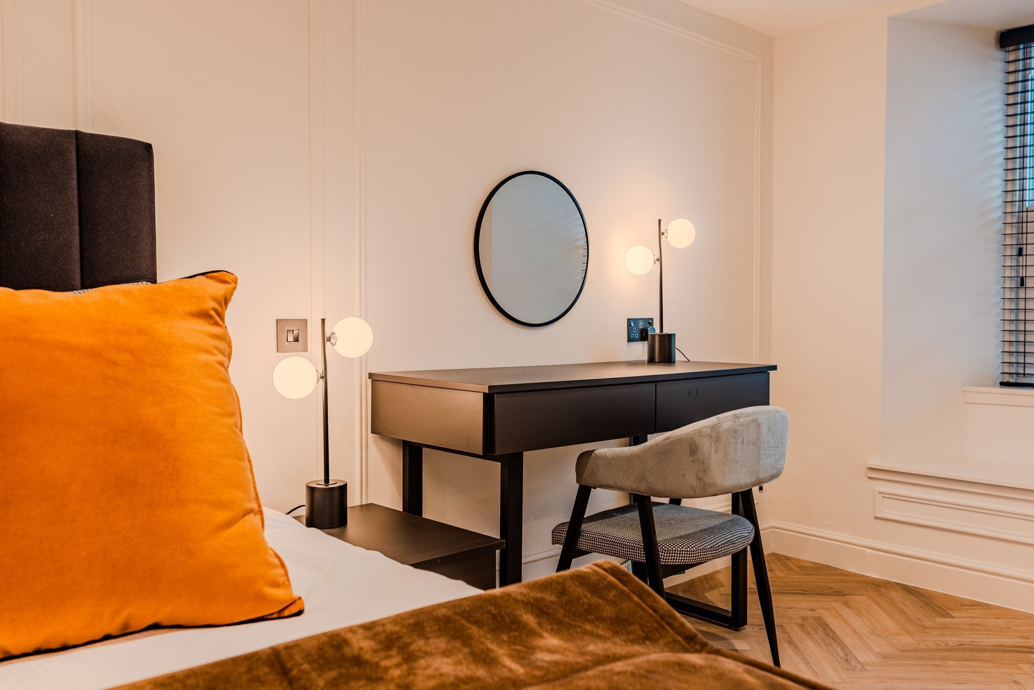 Een moderne slaapkamer met een bed, bureau, stoel en spiegel.
