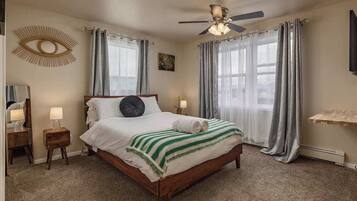 A bedroom with a wooden bed, a ceiling fan, a wall-mounted eye decoration, and a painting.