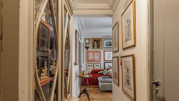 Un couloir avec un canapé rouge, une petite table et divers tableaux encadrés accrochés aux murs.