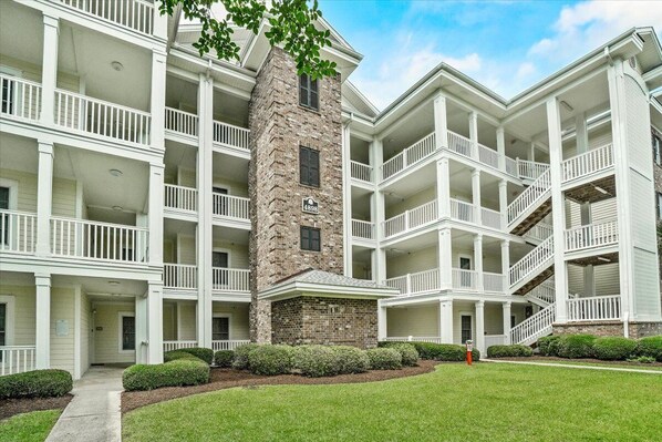 A multi-story building with a central stone tower, multiple balconies, and a well-maintained lawn. - 3-bedroom condo in awesome Myrtle Beach with WiFi, AC (Myrtle Beach)