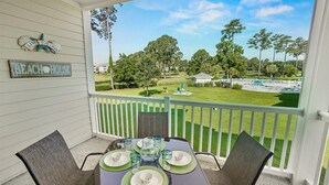 A covered outdoor seating area with a table set for four, overlooking a well-maintained lawn and distant trees.