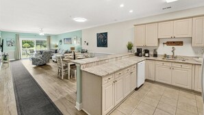 A modern kitchen with a central island, light-colored cabinetry, and a dining area with a sofa and chairs.