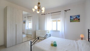 Ein Schlafzimmer mit einem großen Spiegel, einem Kinderbett, einem Bett mit gerollten Handtüchern und einer Chandelier.