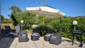 Eine Terrasse im Freien mit Korbmöbeln, einem großen Sonnenschirm und einem Grill.