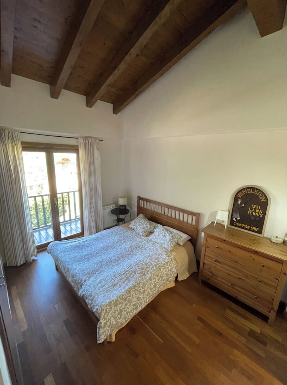 A bedroom with a wooden bed, a dresser, and a window with curtains.