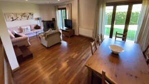Un salon spacieux doté d’un parquet, d’un ensemble de canapés, d’un téléviseur et d’une table à manger avec des chaises.