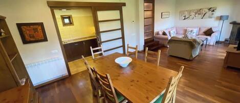 Un comedor con una mesa y sillas de madera, una cocina al fondo y una sala de estar con un sofá y chimenea.