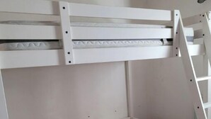 Un lit superposé avec une échelle, un petit banc en bois et un matelas sur le lit du bas.