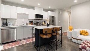 A modern kitchen with white cabinets, a central island with chairs, a built-in oven, and a refrigerator. - 2BR/2BA in the Heart of Ballard (Seattle)