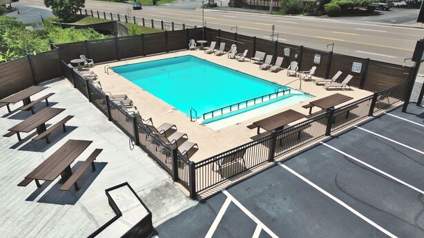 A rectangular swimming pool surrounded by a black fence, with lounge chairs and picnic tables on the deck. - Sleepy Bear Motel (Gatlinburg)