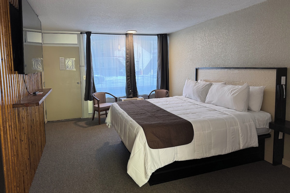 A hotel room with a bed, a desk, a chair, and a large window with curtains.