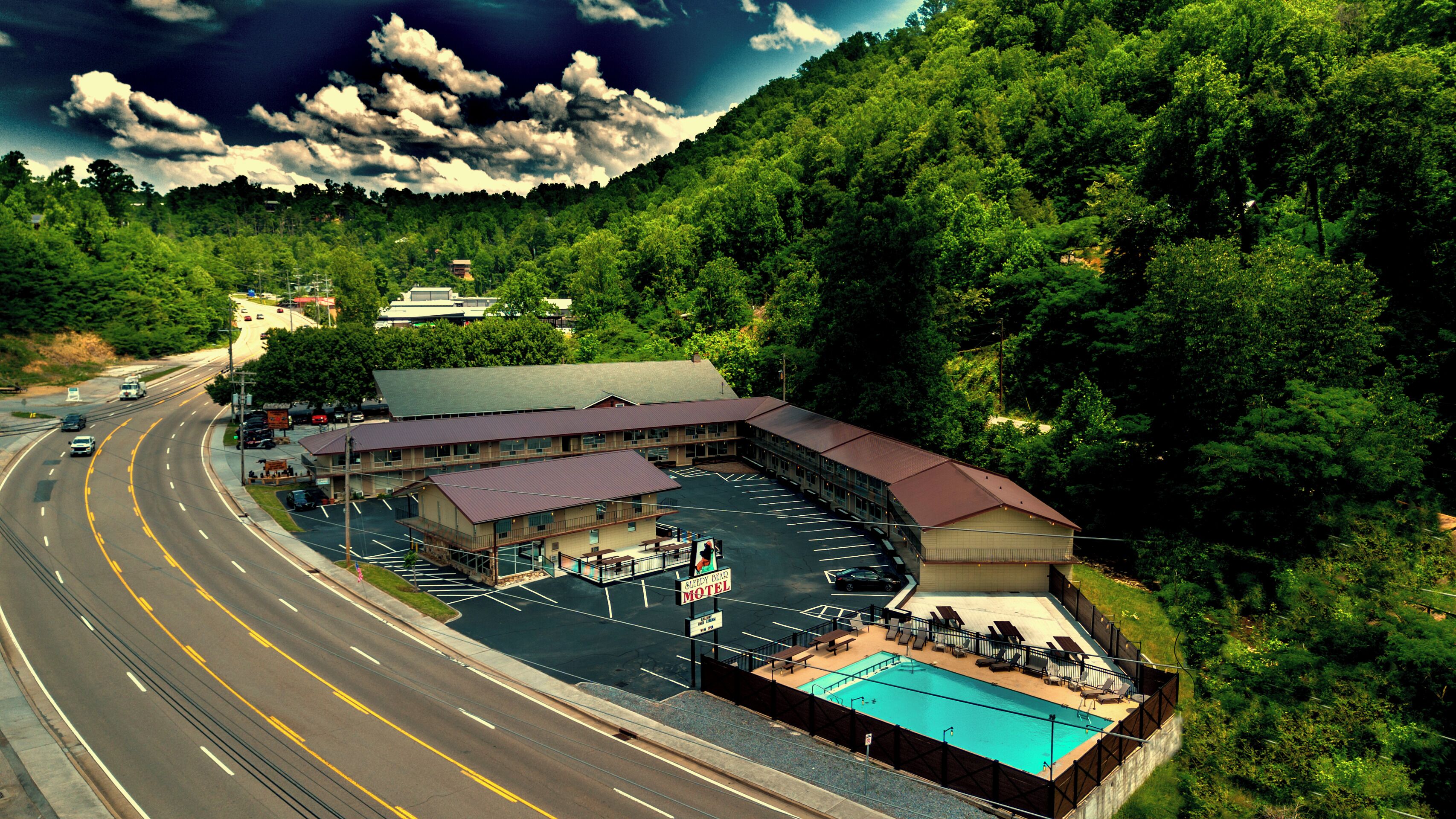 A motel with a swimming pool, a parking lot, and a road with vehicles.