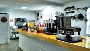 A commercial kitchen with a coffee station, including a coffee machine, various coffee cups, and condiment dispensers. - Sleepy Bear Motel (Gatlinburg)
