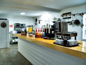 A commercial kitchen with a coffee station, including a coffee machine, various coffee cups, and condiment dispensers. - Sleepy Bear Motel (Gatlinburg)