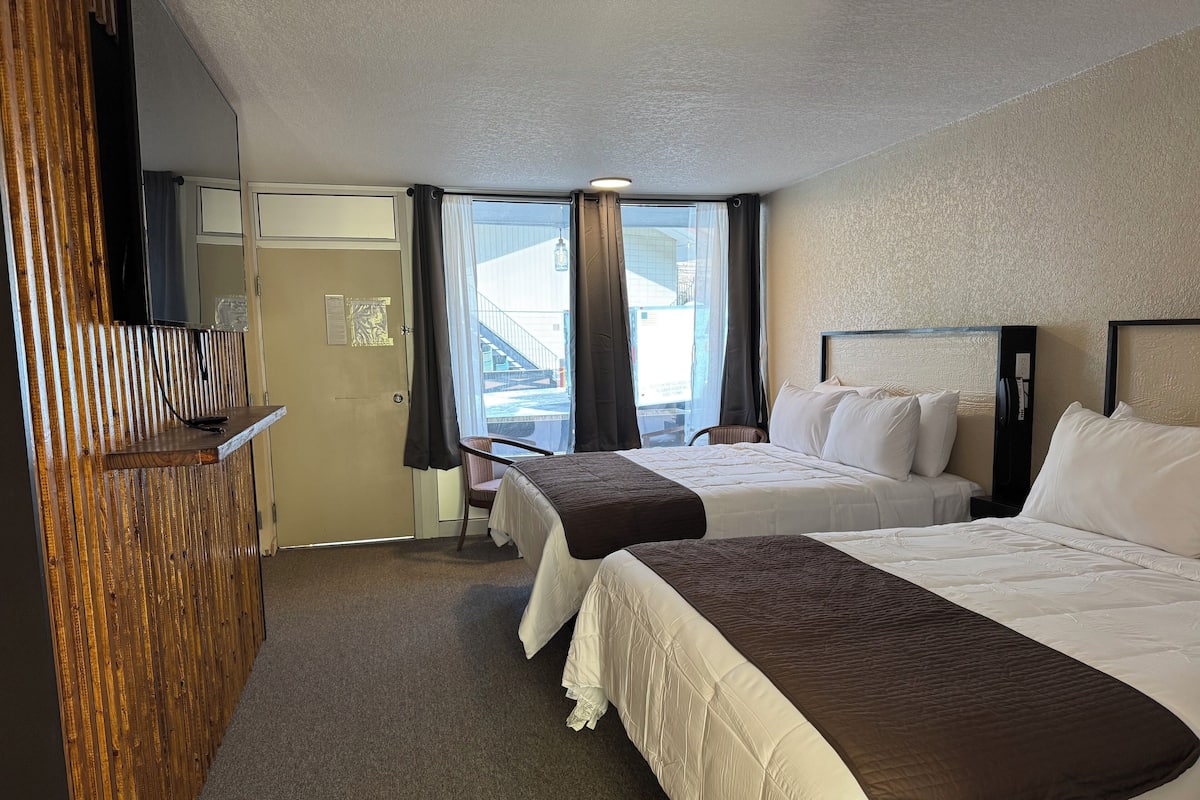 A hotel room with two beds, a desk, a chair, and a large window with curtains.