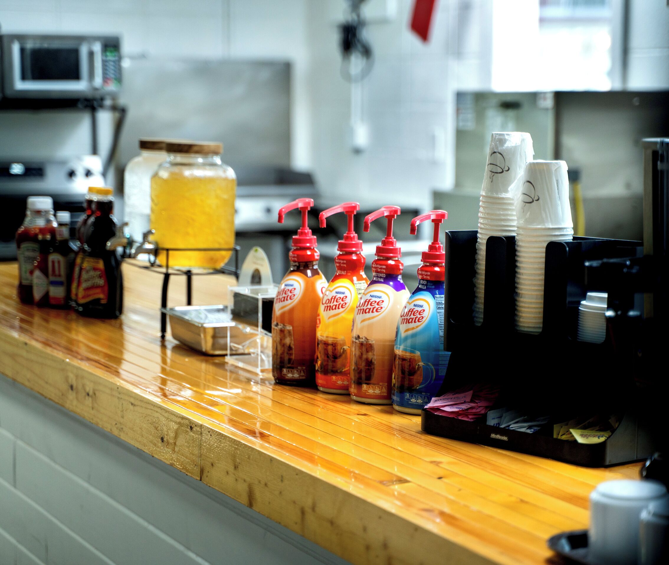 A kitchen counter with coffee-making equipment, including a coffee machine, coffee pods, and condiment bottles.