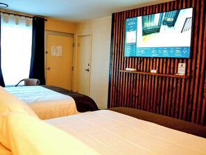 A hotel room with two beds, a TV mounted on a wooden panel wall, and a door with a sign. - Sleepy Bear Motel (Gatlinburg)