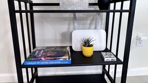 A black metal console table with two shelves, a white vase with white flowers, and a small yellow pot with a plant. - Casa Tuturutu (Willemstad)
