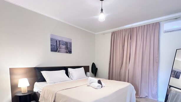 A modern hotel room with a neatly made bed, a bedside lamp, a wall-mounted picture, and a large window with curtains. - Casa Tuturutu (Willemstad)