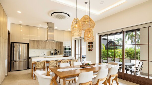 A modern kitchen with stainless steel appliances, a dining area with a wooden table and white chairs, and large windows offering a view of palm trees. - Luxury Beachside Condo in Hacienda Pinilla-Steps from Sand! Beach Club access (Tamarindo)