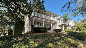 A two-story house with a front porch, a small front yard with ivy, and a clear blue sky.