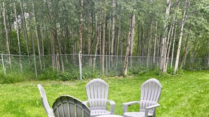 A grassy outdoor area with two Adirondack chairs and a small round table.