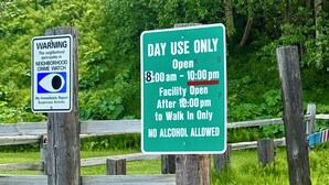 A sign indicating a neighborhood crime watch and a day use only sign with specific opening hours and no alcohol allowed.