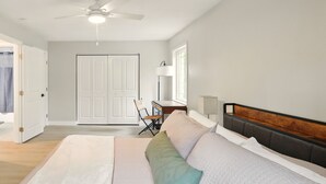 A bedroom with a bed, a desk, a chair, a ceiling fan, and a door.