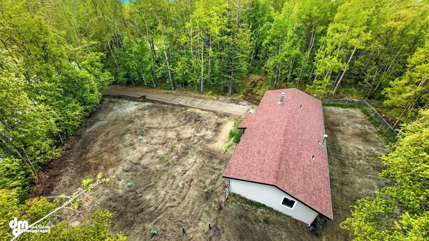 An aerial view of a house with a red roof, surrounded by dense green forest.