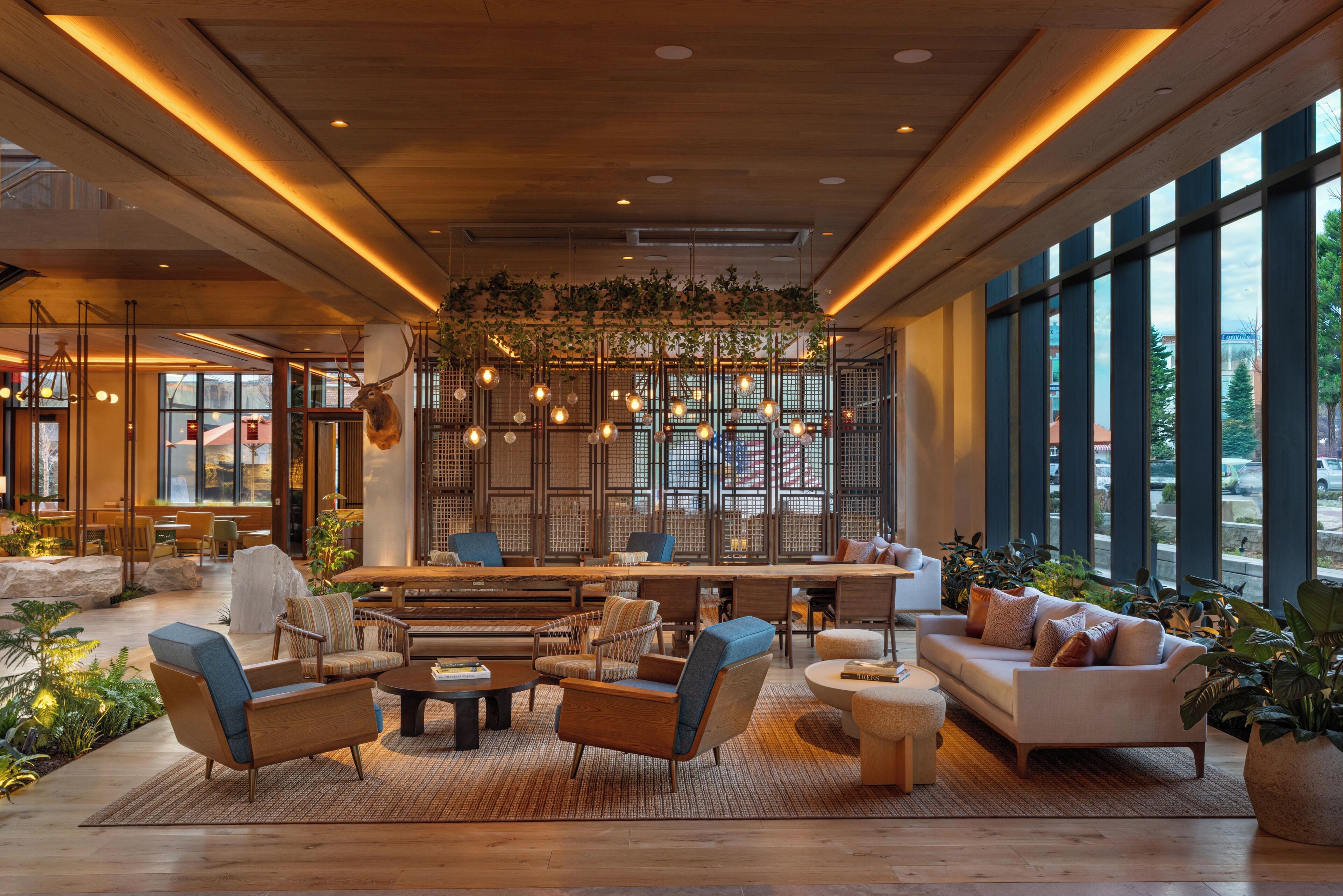 Un hall d’entrée spacieux avec un plafond en bois, de grandes fenêtres et un espace détente comprenant des canapés et des fauteuils.