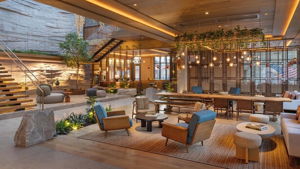 A spacious indoor area with a wooden floor, seating arrangements, a staircase, and a large window. - The Compton (Bentonville)