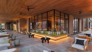 A spacious outdoor seating area with a glass enclosure, wooden furniture, and a brick wall backdrop. - The Compton (Bentonville)