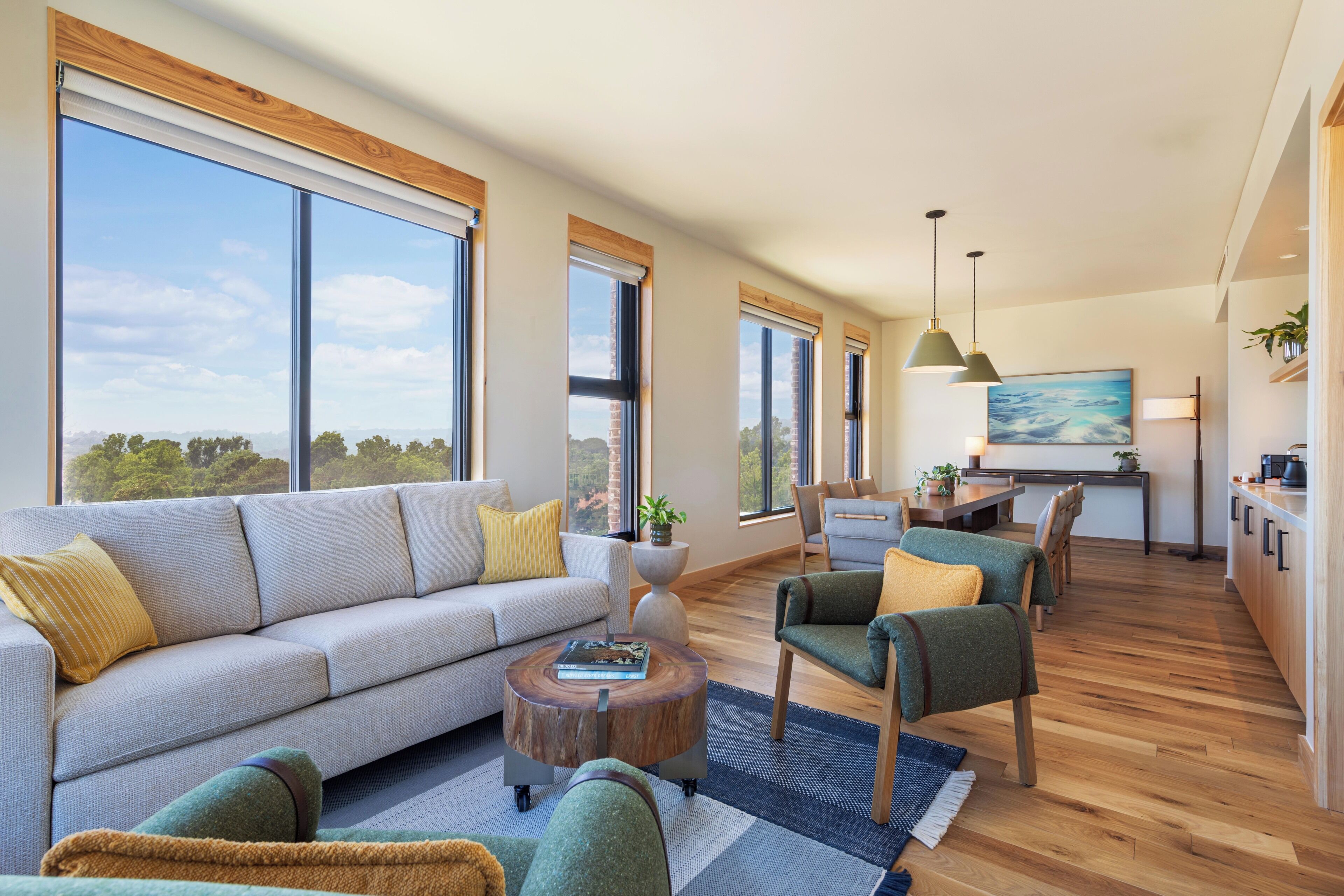 A spacious living area with a sofa, chairs, a round coffee table, and large windows offering a view of the outdoors.
