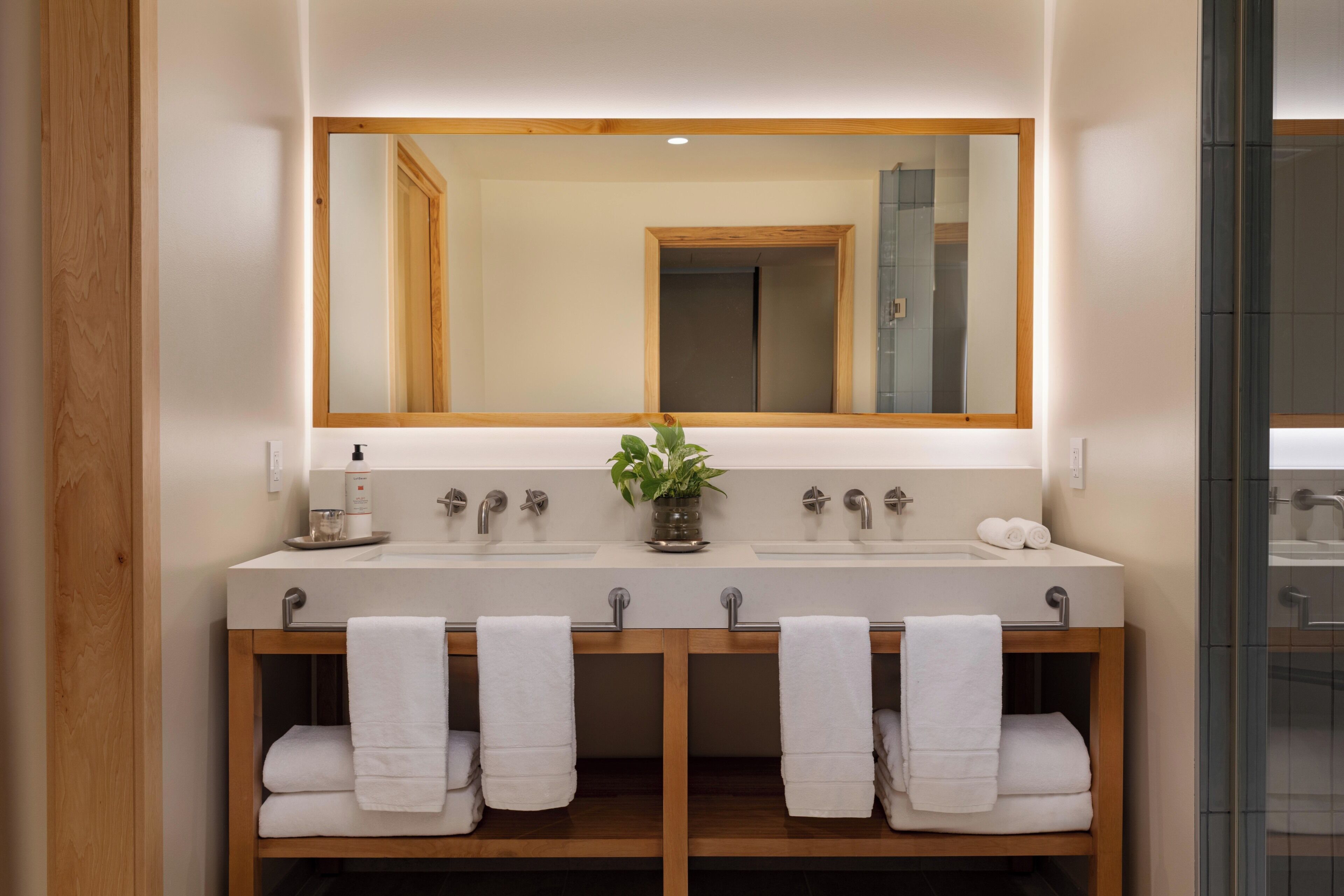 A bathroom with a wooden vanity, two sinks, a large mirror, and a potted plant.