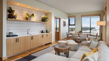 Una cocina moderna con azulejos blancos, armarios de madera y plantas en macetas. Hay una zona de comedor con una mesa y sillas, y un amplio ventanal con vistas.