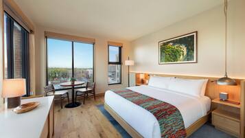 A hotel room with a large bed, a desk, a chair, a table, and a view of the city.
