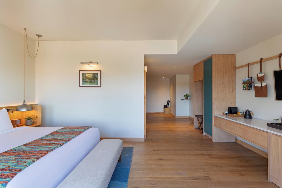 A modern hotel room with a large bed, a desk, and a view into the hallway.