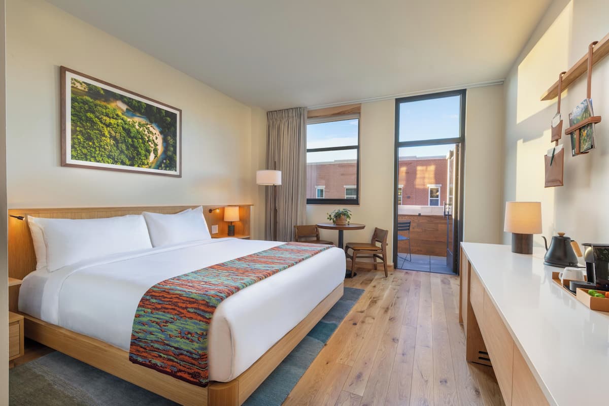A hotel room with a bed, desk, chair, and a large window.
