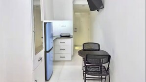 A compact kitchen with a refrigerator, a microwave, and a small dining table with two chairs. - 250 sq.ft 3 Studio Apartment w/ Pool & Private Sauna (Dhaka)
