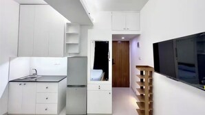 A compact, modern kitchen with white cabinetry, a built-in refrigerator, and a flat-screen TV mounted on the wall. - 250 sq.ft 3 Studio Apartment w/ Pool & Private Sauna (Dhaka)