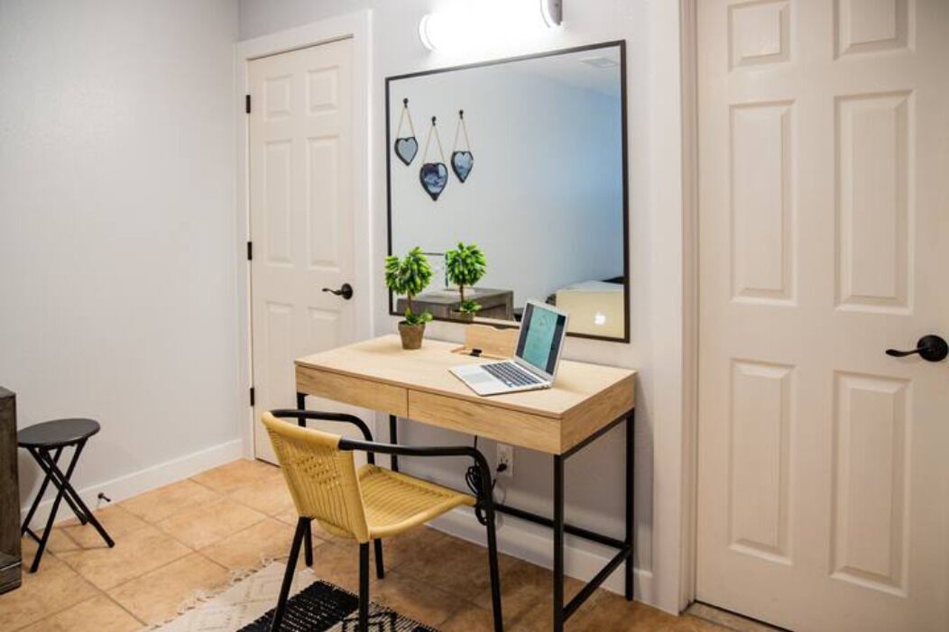 A room with a wooden desk, a laptop, a chair, a small plant, and a mirror on the wall.