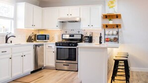 Une cuisine moderne avec des meubles blancs, des appareils en acier inoxydable et un îlot central en bois doté de tabourets.