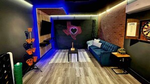 Un salon moderne avec un canapé bleu, un jeu de fléchettes et un cœur lumineux décoratif accroché au mur.