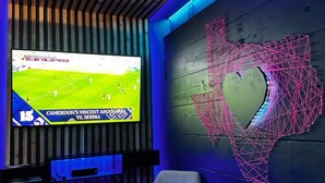 Une pièce avec un téléviseur diffusant un match de sport, un mur en bois orné d’un motif géométrique et un banc.