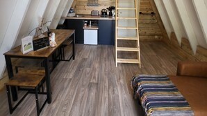 Un dormitorio acogedor en el ático con cama tipo voladizo, un escritorio de madera, una pequeña kitchenette y una escalera.